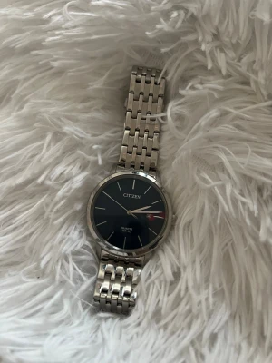 Citizen silverfärgad kloä - Stilren klocka från Citizen med silverfärgad länkarmband och svart urtavla. Klockan har datumvisning och klassisk design med tunna visare och index. Perfekt accessoar för dig som gillar en tidlös look.Finns även mer länkarmar och sätta på ifall den är för liten box ingår.