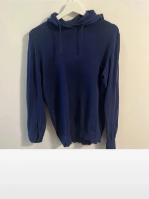 Mörkblå hoodie med huva - En enkel och stilren mörkblå hoodie med huva och dragsko. Hoodien har långa ärmar och ribbade muddar vid ärmslut och nederkant. Perfekt för en avslappnad look och passar till det mesta. Materialet ser ut att vara mjukt och bekvämt, troligen bomull eller bomullsblandning.