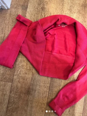 Rosa bolero med sjalkrage - Snygg rosa bolero med bred ribbstickad sjalkrage och muddar. Perfekt att slänga över en topp för en extra touch. Mjuk och stretchig kvalitet, långärmad och kort i modellen.