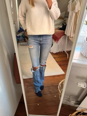 Blå slitna bootcut jeans med hål - Säljer ett par ljusblå bootcut jeans med stora slitningar och hål på knäna. Jeansen har klassisk femficksdesign och råa kanter vid hålen. Perfekt för dig som gillar en avslappnad och trendig look. Högmidjade! 💟