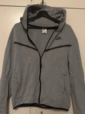 Grå Nike Tech -  klassisk grå Nike Tech. Riktigt stilren och passar bra med de flesta plaggen.