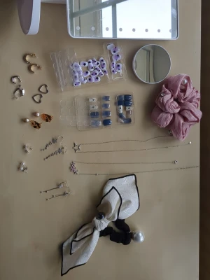 Mixade örhängen, halsband, spegel osv  - Säljer ett set med flera olika örhängen i både silver- och guldfärg, även mycket annat. Säljer  två halsband i silverfärg med tillhörande örhängen. Även två olika håraccessoarer med fina detaljer. Två kit lösnaglar (press on) med klister till (kan ej förmoda att klistret är bra). Säljer även en sminkspegel med en liten spegel till (kan dock ej förmoda att ljuset funkar till spegeln). Två par örhängen längst till vänster är från KappAhl och snöflingorna är från glitter. Pris kan diskuteras:)