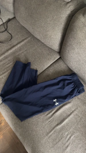 Marinblå mjukisbyxor Under Armour - Säljer ett par marinblå mjukisbyxor från Under Armour med resår i midjan och logga på benet. Byxorna har en avslappnad passform och är tillverkade i ett lätt och mjukt material som passar perfekt för chill eller träning.