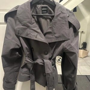 Kort grå trenchcoat från Bershka - Stilren populär trenchcoat från Bershka med knytskärp i midjan. Storlek S🩷
