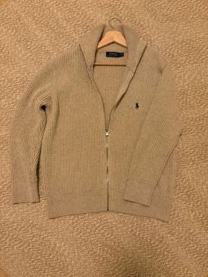 Ralph Lauren full zip cardigan  - Säljer detta sjukt feta Ralph Lauren plagget. Grymt skick, använd sparsamt 4-5 gånger. Storlek M, färg beige, sjukt snygg och stilren. Hör av er vid frågor/ fler bilder! 