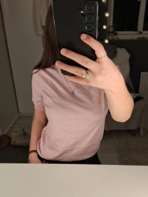 Ljusrosa kortärmad topp - En enkel och stilren ljusrosa topp från LINDEX med rund halsringning och korta ärmar. Perfekt att matcha med jeans eller kjol för en avslappnad look. En liten defekt på framsidan.