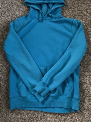 Blå hoodie från 157 med huva - Säljer en blå hoodie från 157 i storlek S. Hoodien har en klassisk huva med dragsko och en stor magficka framtill. Tillverkad i mjukt material som passar perfekt för chill dagar. Enkel och stilren design utan tryck eller mönster.