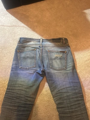 Blåa selvedge nudie jeans - Säljer ett par blå jeans från nudie med feta slitningar på både fram- och baksida. Jeansen har klassisk femficksdesign, raka ben och detaljerade sömmar. Perfekta för en avslappnad och trendig look. Jeansen har använts i ungefär ett och ett halvt år och dom passar ungefär 170cm. Om någon har frågor så fråga bara.