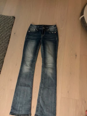 Miss me jeans stl 26 - Säljer mid waist bootcut miss me jeans i stl 26, de är i bra skick. Bara använda ett fåtal gånger. Jag är 170 och de släpar lite i marken. De har coola detaljer både bak och fram. Kontakta mig om du har några frågor.