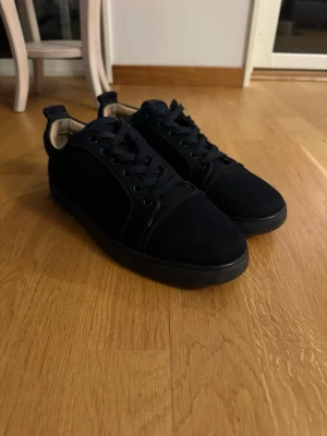 Mörkblåa Louboutin  - Stilrena blå sneakers med lågt skaft och röd yttersula. Skorna har blåa skosnören och ovandel i mockaliknande material. Perfekta för dig som vill ha en clean look med en twist. Passar till det mesta och är riktigt bekväma.