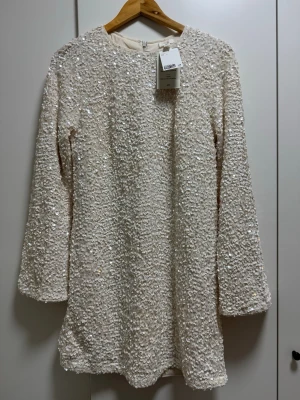 Paljettklänning i ljusbeige  - Säljer en superfin ljusbeige kortklänning täckt med glittriga paljetter.  Dragkedja bak för enkel påklädning. Storlek S men passar M