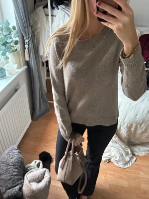 Beige stickad tröja med rund hals - Mysig beige stickad tröja med rund halsringning och ribbade muddar vid ärmslut och nederkant. Tröjan har en avslappnad passform och är perfekt för lager på lager. Enkel och stilren design som passar till det mesta.