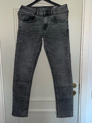 Grå slim fit jeans med hög midja - Snygga grå slim fit jeans med hög midja och klassisk femficksdesign. Jeansen har raka ben och svarta sömmar som ger en clean look. Tillverkade i stretchigt denimtyg för extra komfort. Perfekta för dig som gillar en stilren och modern vibe.