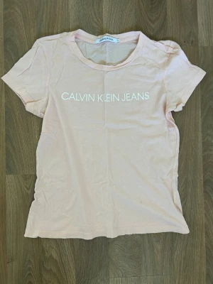 Ljusrosa Calvin Klein Jeans t-shirt - Snygg ljusrosa t-shirt från Calvin Klein Jeans med vit logga på bröstet. Finns en liten fläck framtill, se bild, ej provat behandla. Djur och rökfritt hem.
