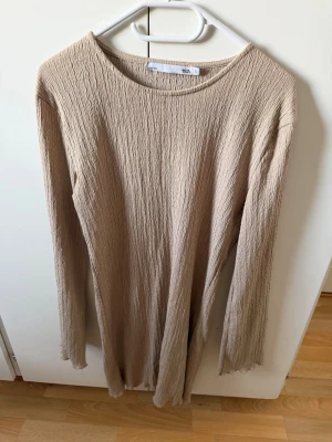 Beige långärmad klänning  - Beige långärmad klänning från lager 157 i ett krinklat, strukturerat tyg. Klänningen har rund halsringning och rak passform som ger en avslappnad look. Perfekt för dig som gillar minimalistisk stil och mjuka material.