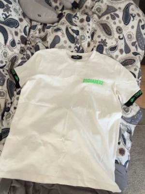 DSQUARED2 t-shirt  - Vit t-shirt från DSQUARED2 med grönt logotryck på bröstet och svarta detaljer med grön text på ärmarna. Klassisk passform och rund halsringning. Perfekt för en trendig och avslappnad stil.