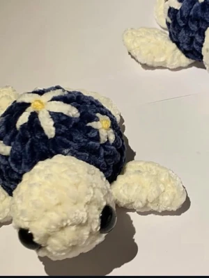 Mjukis-sköldpadda med blommor - Söt handgjord mjukis-sköldpadda i vit och mörkblå plysch med broderade vita och gula blommor på skalet. Sköldpaddan har stora svarta ögon och är perfekt som dekoration eller gosedjur.