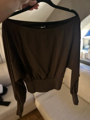 Brun asymmetrisk långärmad topp från Gina Tricot - Brun långärmad topp från Gina Tricot med bred mudd i midjan och vid ärmslut. Toppen har en lösare passform upptill och är asymmetrisk. 