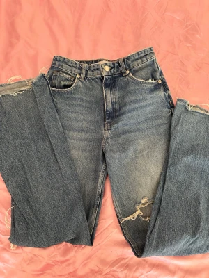 Zara straight leg high/mid rise jeans with slits (s-m) - Säljer ett par blå mom jeans med hög midja och stora slitningar vid knäna. Jeansen har klassisk femficksdesign och raka ben. Perfekta för en avslappnad och trendig look. Materialet är kraftig denim i bomull.