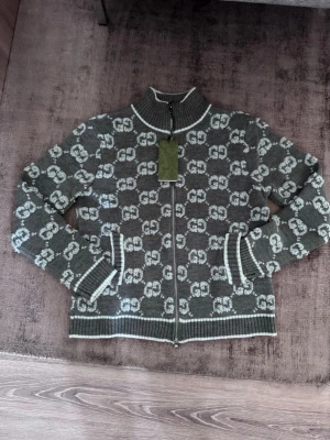  Gucci zip up  - Snygg grå stickad ziptröja från Gucci med vitt GG-mönster över hela tröjan. Tröjan har hög krage, hel dragkedja och ribbade muddar samt nederkant med vita ränder. Perfekt för dig som gillar exklusiv streetstyle. Stl S jätte fint skick och extremt skön. Priset går att diskuteras vid snabb affär 