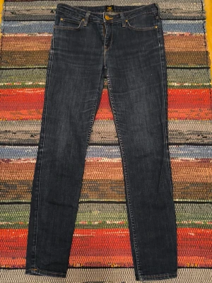 Lee Scarlett jeans W29 L31 – mörkblå stretch - Säljer ett par Lee Scarlett. Mörkblå tvättad stretch-denim med karaktäristisk guldgul sömstickning och klassiskt Lee-märke på baksidan. Bra skick med normalt brukslitage. Visst slitage vid grenskudden – se bild.