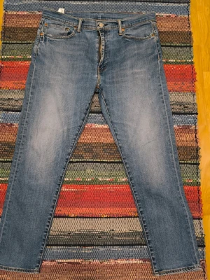 Levi's 512 blå jeans, storlek W36 L30 - Ett par Levi's 512 ljusblå jeans. Jeansen har en klassisk design med fem fickor, gylf med dragkedja och knappstängning. Snyggt patinerade, lite naggade i ena fickan som syns på bild.
