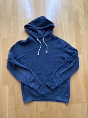 Pier one hoodie - En stilren mörkblå hoodie med klassisk huva och vita dragsnören. Hoodien har en magficka framtill och ribbade muddar vid ärmar och nederkant. Perfekt för en avslappnad look och enkel att matcha med jeans eller joggers.