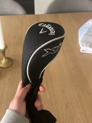 Callaway XJ svart golfklubbskydd - Säljer ett svart golfklubbskydd från Callaway XJ-serien. Skyddet har vita detaljer, broderad logga och texten 'FW' på ovansidan. Materialet är en kombination av textil och stretchigt tyg som gör det enkelt att trä på klubban. Perfekt för att skydda din fairwaywood.