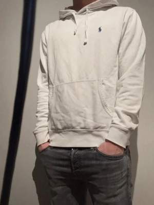 Vit hoodie från Polo Ralph Lauren🤩🙌 - Snygg vit hoodie från Polo Ralph Lauren med klassisk blå logga på bröstet. Hoodien har huva med dragsko och en stor känguruficka framtill. Perfekt för en avslappnad och stilren look.🙌