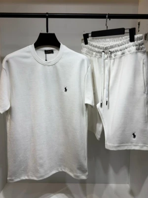 Ralph Lauren Set - Snyggt vitt set från Polo Ralph Lauren med t-shirt och shorts. Båda plaggen har den klassiska broderade loggan i svart. T-shirten har rund hals och kort ärm, shortsen har resår i midjan och dragsko. Perfekt för en avslappnad och stilren look.