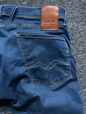 Blå Replay Hyperflex jeans Anbass - Snygga blå jeans från Replay, modell Anbass Hyperflex. Klassisk femficksdesign med ljus kontrastsöm och läderpatch bak i midjan. Stretchigt material för extra komfort och passform. Perfekta för en trendig och avslappnad look.