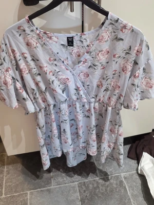 Blommig omlottklänning från SHEIN - Superfin ljusblå omlottklänning från SHEIN Curve med blommigt mönster i rosa och grönt. Klänningen har korta ärmar, v-ringning och en avslappnad passform som ger en romantisk vibe. Perfekt för varma dagar och somriga tillfällen.