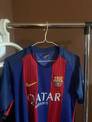 FC Barcelona matchtröja Nike - Säljer en klassisk FC Barcelona matchtröja från Nike i blått och rött med klubbmärke, Qatar Airways-tryck och gul Nike-logga. Tröjan har korta ärmar och sponsortryck på ärmen. Perfekt för dig som älskar fotboll och Barca
