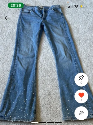 Blå bootcut jeans med pärldetaljer - Snygga blå bootcut jeans med pärldetaljer nertill på benen. Klassisk femficksmodell och normalhög midja. Perfekta för dig som vill ha en unik touch på dina jeans. Jeansens material är klassisk denim i bomull.