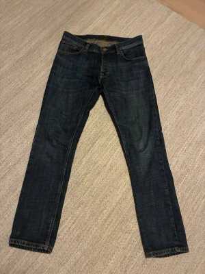 Mörkblå slim fit jeans - Snygga mörkblå slim fit jeans med klassisk femficksdesign och kontrastsömmar. Jeansen har en läderpatch bak i midjan och är tillverkade i ett stretchigt denimtyg som ger en skön passform. Perfekta för dig som gillar en stilren och enkel look. Helt nya och snygga i perfekt skick