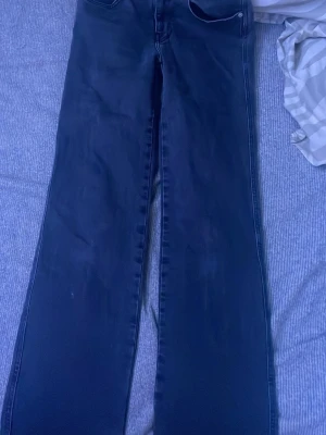 Svart/gråa  bootcut jeans - Säljer ett par mörkblå bootcut jeans med klassisk femficksdesign och medel hög midja. Under naveln. Jeansen har raka ben som blir vidare nedtill och är tillverkade i ett stretchigt denimtyg. Perfekta för dig som gillar en retroinspirerad look. Använda några gånger därfer slitning vid botten som ni ser i en av bilderna. Säljer då jag inte använder dom 