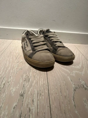 Saint Laurent stl 40  - Säljer ett par grå saint Laurent skor i stl 40. Skorna är i helt okej skick men skulle behöva en vända hos skomakaren eftersom sulan har släppt lite där fram, därför säljer jag de billigt. De är också slitna i hälen. 