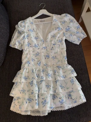 RESERVERAD!! - Säljer denna superfina klänning i vitt med blått blommönster. Den är endast använd en gång!