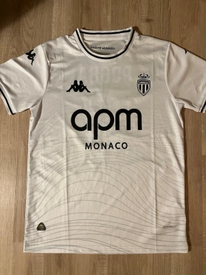AS Monaco Pogba matchtröja vit - Snygg vit AS Monaco matchtröja med Pogba och nummer 8 på ryggen. Tröjan har svarta detaljer, klubbmärke och sponsortryck framtill. Tillverkad i lätt och ventilerande material, perfekt för fotboll eller träning.