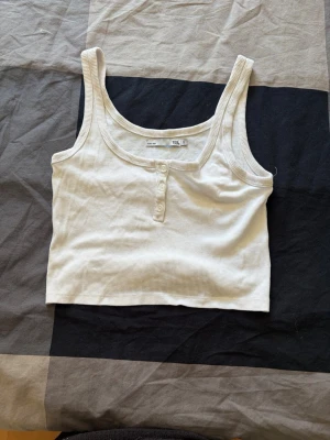 Vit ribbad croppad linnetopp - Säljer en vit ribbad croppad linnetopp från H&M med knappar framtill. Toppen är ärmlös och har breda axelband, perfekt för varma dagar eller som lager på lager-plagg.