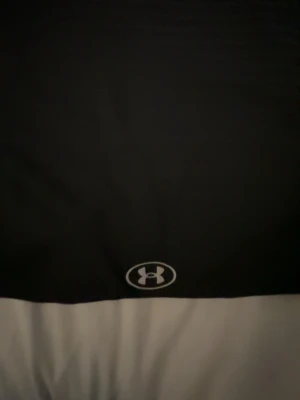 Svart träningströja från Under Armour - Snygg svart träningströja från Under Armour med rund hals och diskret logga på bröstet. Tillverkad i ett lätt och snabbtorkande material som passar perfekt för gymmet eller löpning. Klassisk passform och stilren design.