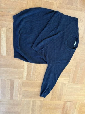 Mörkblå stickad tröja Kappahl - Mörkblå stickad tröja från Kappahl med rund halsringning och ribbade muddar. Tröjan har en klassisk, avslappnad passform och är tillverkad i ett mjukt, grovstickat material som passar perfekt för kyligare dagar.