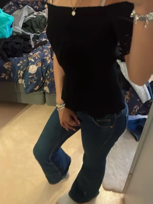 Svart offshoulder topp - Snygg svart offshoulder topp med smickrande passform. Toppen är ärmlös och har en enkel, stilren design som passar perfekt till jeans eller kjol. Perfekt för dig som vill ha en trendig och stilren look.