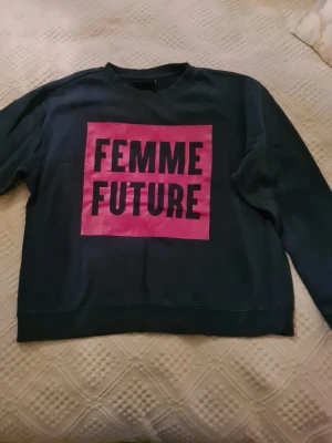 Mörkgrön sweatshirt Monki Femme Future - Cool mörkgrön sweatshirt från Monki med trycket 'FEMME FUTURE' i mörkgrön på en rosa ruta framtill. Tröjan har rund halsringning och långa ärmar. Perfekt för dig som vill sticka ut med ett statement-plagg. Mjuk insida och avslappnad passform.