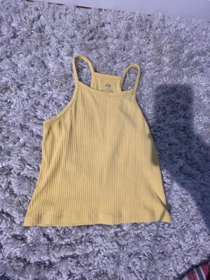 Gul ribbad linnetopp från H&M - Snygg ljusgul ribbad linnetopp från H&M med smala axelband och rak passform. Perfekt för varma dagar och enkel att styla med jeans eller kjol. Tillverkad i mjuk bomull för skön känsla.