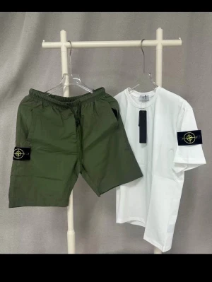 Stone Island set med shorts och t-shirt - Snyggt set från Stone Island med vita t-shirten och gröna shorts. Båda plaggen har den ikoniska Stone Island-loggan på ärm och ben. T-shirten är enkel och stilren, shortsen har resår i midjan och praktiska fickor. Perfekt för en avslappnad och trendig look.