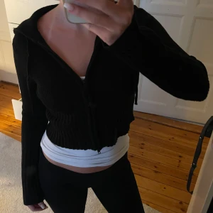Stickad zip up kofta  - Svart stickad zip up kofta i ribbat tyg. Har luva och dragkedja. Ganska croppad i modellen. Mycket bra skick.