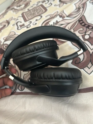 Svarta over-ear hörlurar - Snygga svarta over-ear hörlurar med vadderade kåpor och justerbart huvudband. Hörlurarna har vikbar design och mjuka öronkuddar i konstläder för extra komfort. Perfekta för musik, gaming eller videos. Sladdanslutning och knapp på sidan.