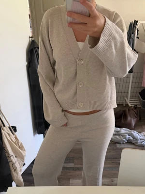 Beige loungewear-set med kofta - Mysigt loungewear-set i beige med en ribbstickad kofta med stora knappar och matchande byxor med utsvängda ben. Perfekt för chill dagar hemma. Mjukt material och avslappnad passform.