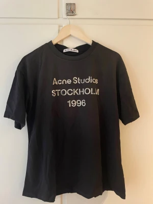 Svart Acne Studios t-shirt Stockholm - Snygg svart t-shirt från Acne Studios med tryck 'Acne Studios STOCKHOLM 1996' på bröstet. Klassisk passform och rund hals. Perfekt till jeans eller shorts för en clean och stilren look.